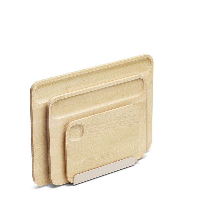 The Caraway 4 Piece Cutting Board Set by Caraway features non-toxic, FSC-certified birch wood boards stacked upright in a sleek metal holder, all displayed against a plain white background.