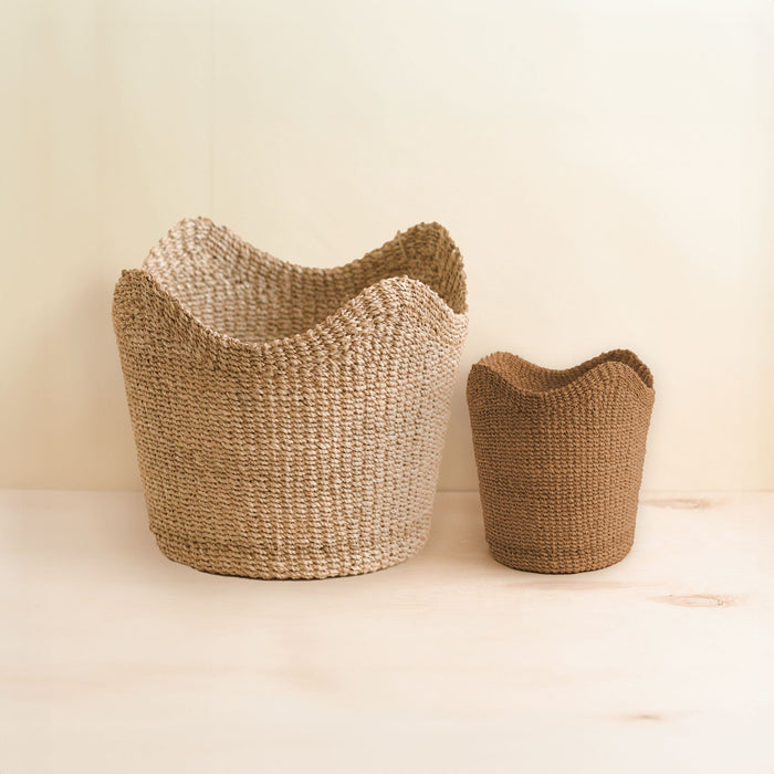 The LIKHA Abaca Small Scallop Basket sits beside a large, light beige basket on a light wooden surface, set against a neutral background.