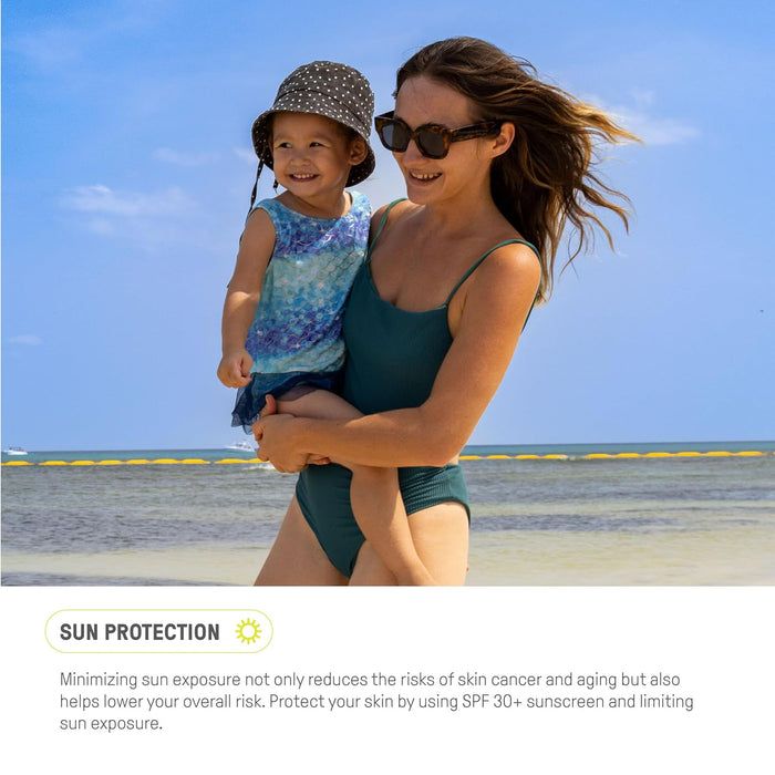 A woman in a swimsuit holds a smiling child in a hat by the beach. Both wear sunglasses, enjoying the clear sky and calm sea. Text at the bottom emphasizes gentle protection with Raw Elements Baby + Kids Lotion Tin SPF 30, highlighting its importance for sun safety.