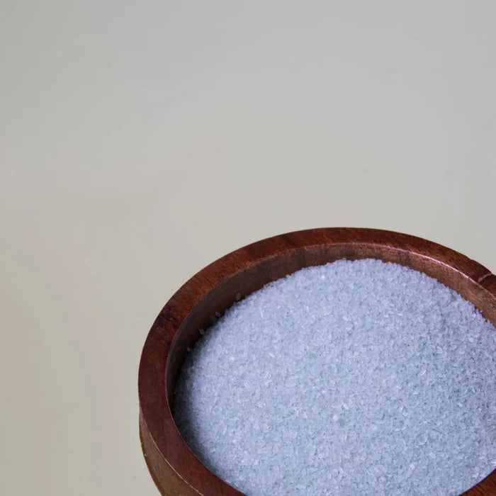 A wooden bowl filled with Pacha Soap Co. Breathe Salt Soak Epsom salt granules sits in the lower right corner against a plain, light-colored background.