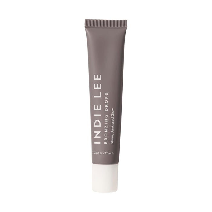 A taupe tube of Indie Lee Bronzing Drops with a white cap stands upright. The label says Indie Lee Bronzing Drops, a bronzing serum for a natural sun-kissed glow. The tube contains 20 ml (0.68 fl oz).