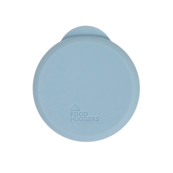 A round, light blue reusable silicone Can Hugger has a small tab and features the Food Huggers logo in the center.
