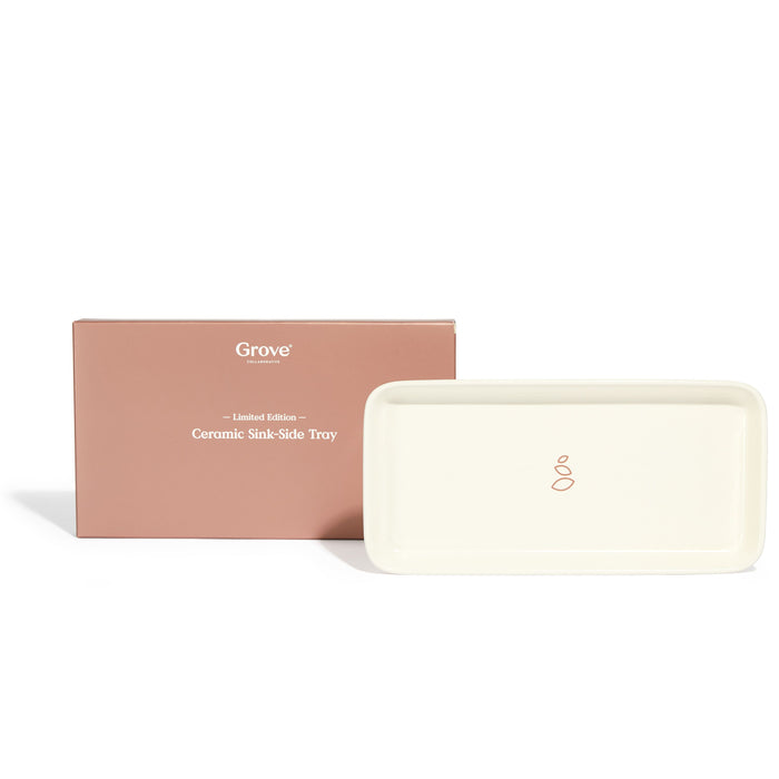 The Grove Co. Ceramic Sink-Side Tray, an exclusive bathroom accessory, comes in a brown packaging box labeled Grove Limited Edition Ceramic Sink-Side Tray. This rectangular tray has smooth edges and a minimalist design logo at the center.