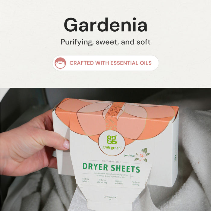 A hand places a box of grab green Classic Dryer Sheets - Gardenia - NEW, featuring purifying, sweet, and soft qualities with essential oils to soften clothes and reduce static cling, into the dryer. A white towel is inside the dryer.