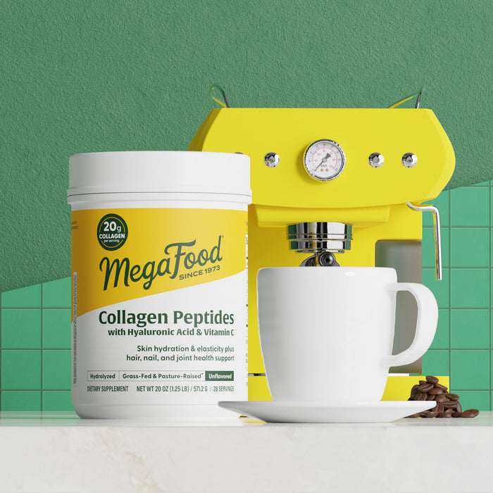 A container of MegaFood Collagen Peptides Unflavored sits by a white coffee cup and yellow espresso machine on a green-tiled counter. Scattered coffee beans highlight the ideal pairing for your daily hydrolyzed collagen boost.
