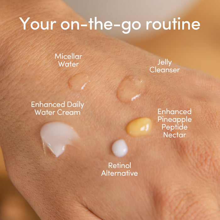 A close-up of a hand holding five Uncommon Beauty essentials—Micellar Water, Jelly Cleanser, Enhanced Daily Water Cream, Pineapple Peptide Nectar, and Retinol Alternative—from the Daily Skincare Travel Set.