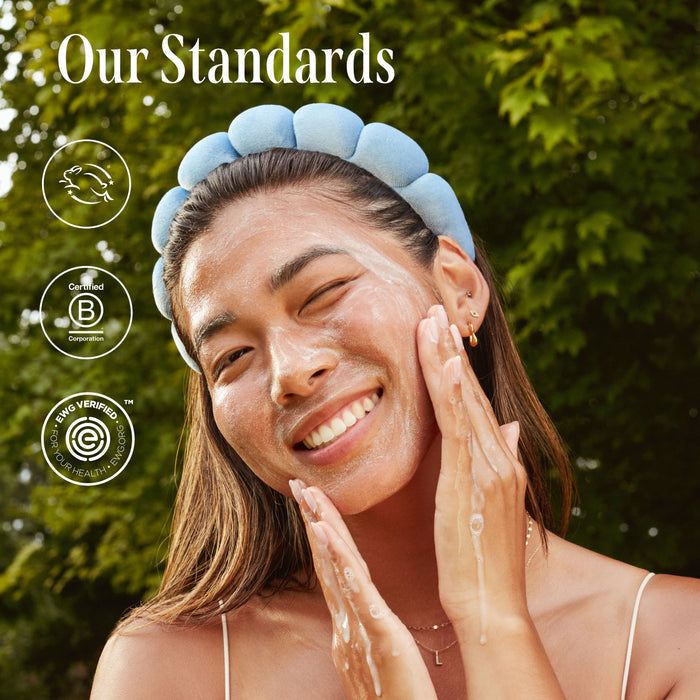 A smiling person with a blue headband applies Three Ships Dream Bio-Retinol + Shorea Butter Rejuvenating Cream outdoors, green trees behind them. Text says Our Standards with three certification icons on the left side.