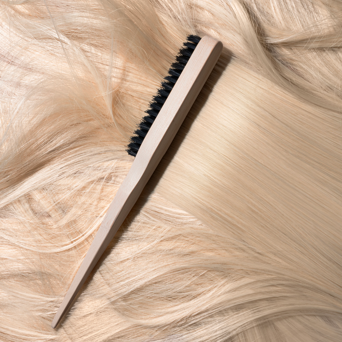 An EcoTools Eco Slick Back Brush with a renewable bamboo handle lies on flowing light blonde hair. Its vegan boar bristles contrast with the smooth texture of the handle, forming a harmonious composition.