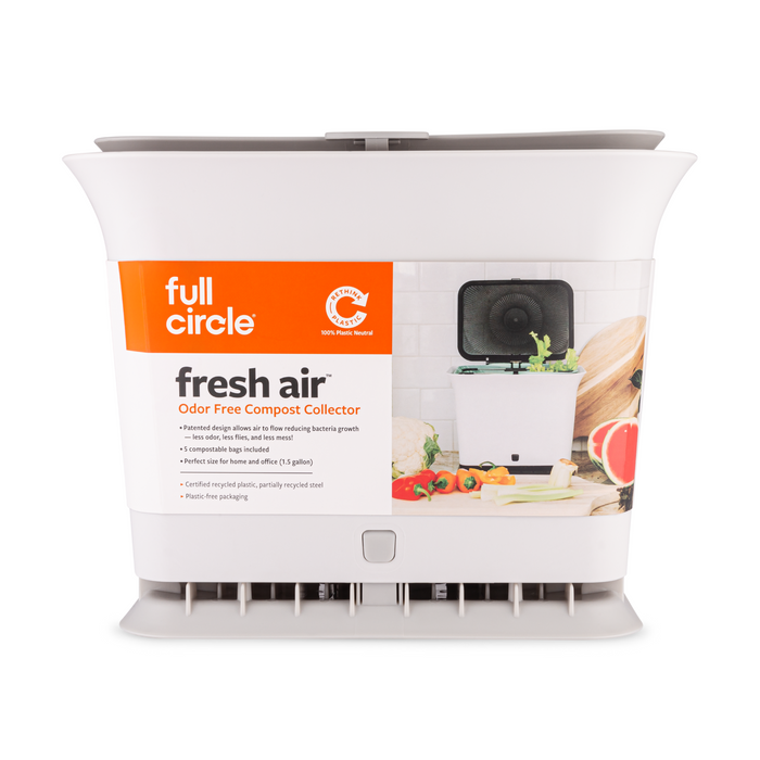 A white Full Circle Fresh Air Compost Bin sits on a kitchen counter beside fresh produce. This 1.5-gallon, stink-free kitchen waste collector reduces odors and features a clearly marked label.