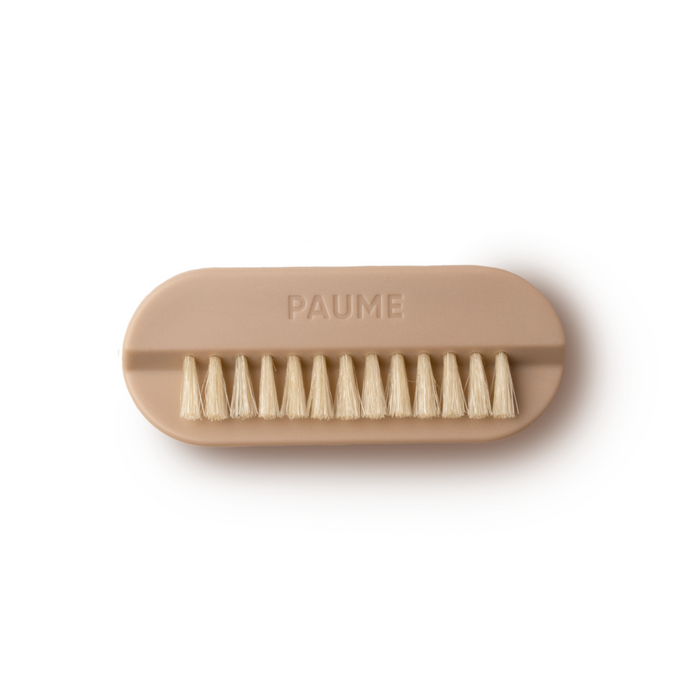 The PAUME Hand & Nail Brush, featuring natural boar bristles, offers a rejuvenating dry brush experience with its beige oval shape and compact design, perfect for luxurious hand care. Positioned against a plain white background, it adds an elegant touch to your cleaning routine.