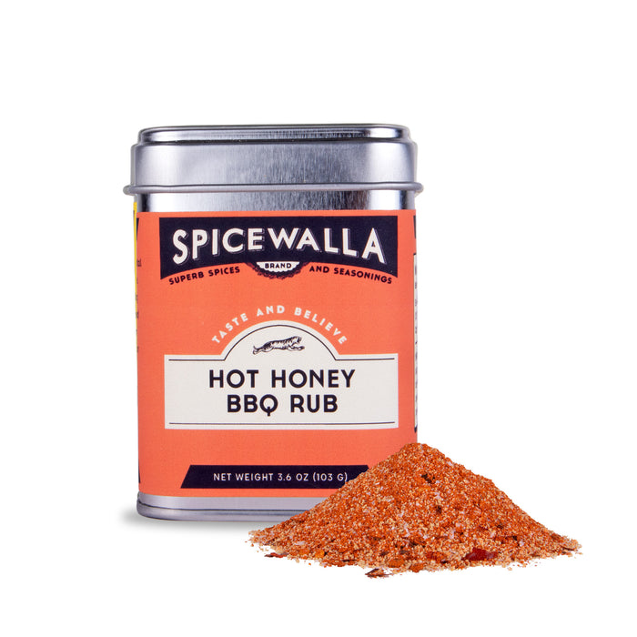 A Spicewalla Hot Honey BBQ Rub tin sits beside a small pile of the spicy, reddish-orange blend with a touch of brown sugar, shown against a white background.