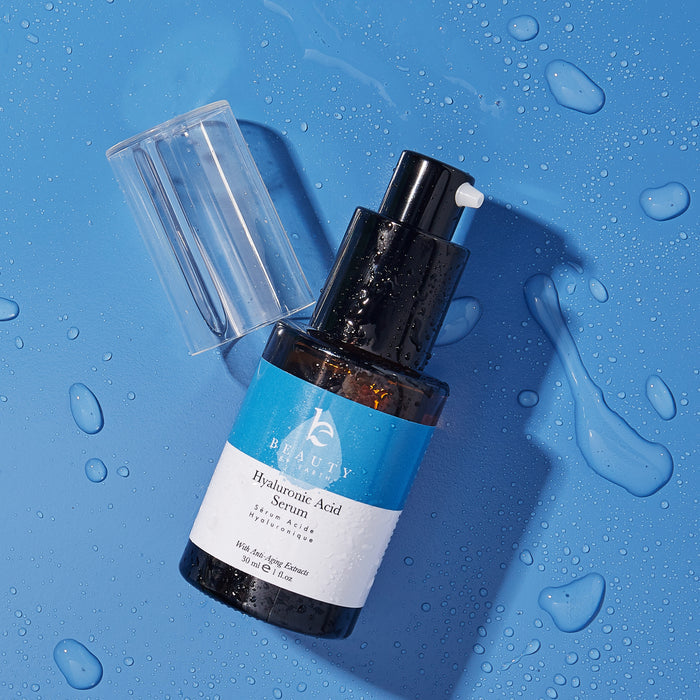 A Beauty by Earth Hyaluronic Acid Serum bottle with a blue label and black pump top sits on a blue surface, its clear cap removed. Water droplets add freshness, promising hydrating effects for a youthful glow.