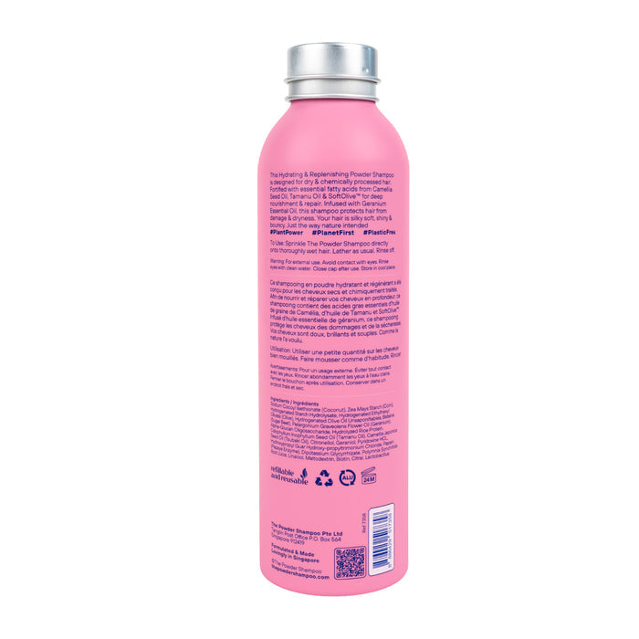 A pink bottle of The Powder Shampoos Hydrating & Replenishing Powder Shampoo showcases its back label with text and symbols. This powder-to-foam shampoo in a shiny silver-capped container is ideal for hydrating moisture to chemically processed hair.