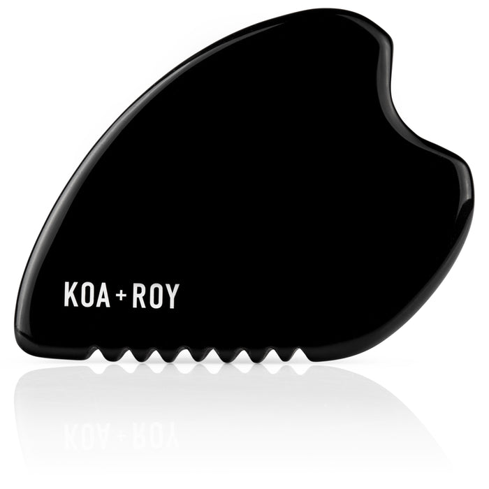 The KOA + ROY Large Black Obsidian Body Gua Sha Tool features a curved, wavy shape and “KOA + ROY” in white on its smooth surface—ideal for lymphatic drainage inspired by traditional Chinese medicine.