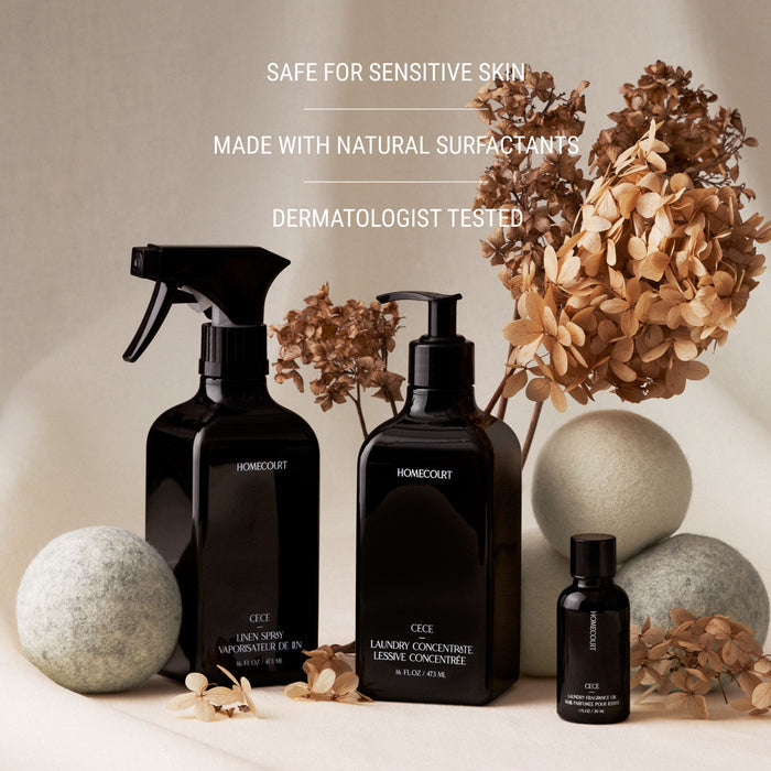 Three black bottles of Homecourt Linen Spray are arranged with dried hydrangeas and decorative stones on a beige surface. Text above reads: Safe for sensitive skin, made with eco-friendly ingredients, dermatologist tested.