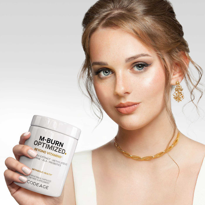 A woman with light brown hair in a white top and gold jewelry elegantly holds Codeages M-Burn Optimized dietary supplement, infused with decaffeinated green tea extract, as she poses against a plain background.