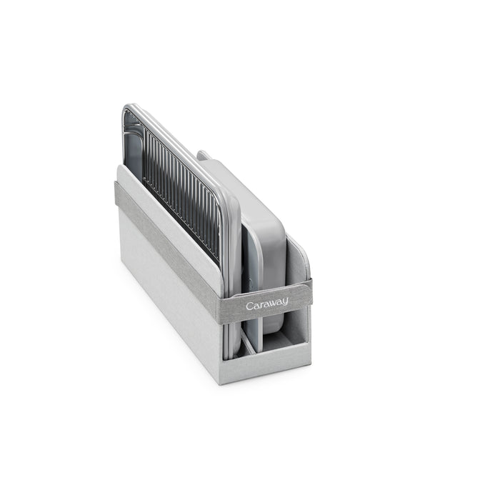The Caraway Mini Bakeware Set with Storage features gray and silver ceramic-coated baking sheets and pans, neatly organized upright in a matching gray storage caddy, all set against a plain white background.