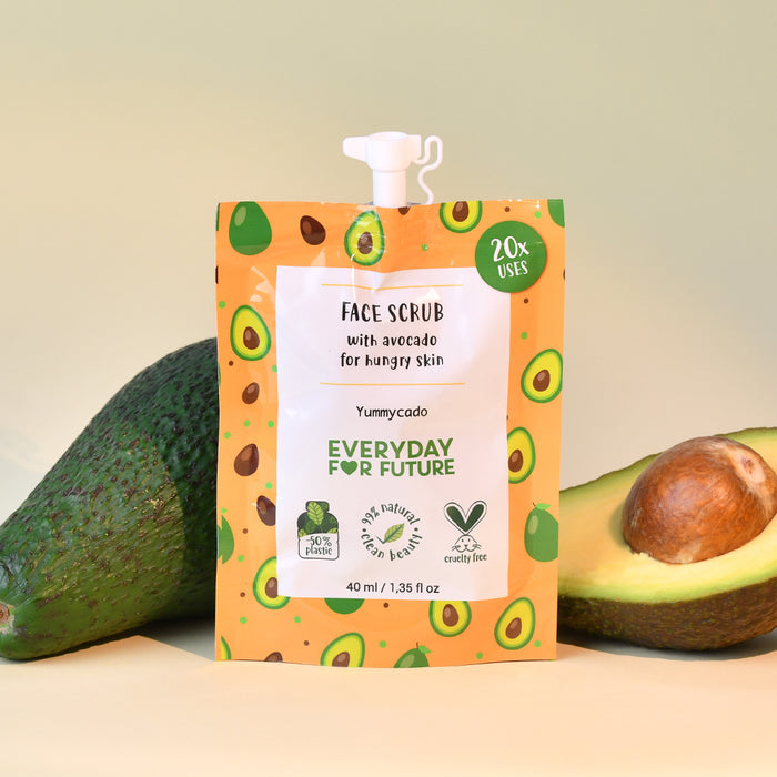 The Nourishing Avocado Face Scrub by Everyday For Future elegantly sits among a whole avocado and a sliced half. Its orange packaging, featuring avocado illustrations, emphasizes natural ingredients and cruelty-free benefits—ideal for your skincare routine.