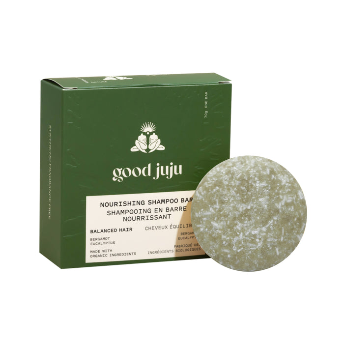 A round, greenish shampoo bar sits before a green Good Juju Body & Home box labeled "Nourishing Shampoo Bar for Balanced/Normal Hair," featuring white and beige text plus a botanical design—an ideal pick for natural hair care with organic ingredients.