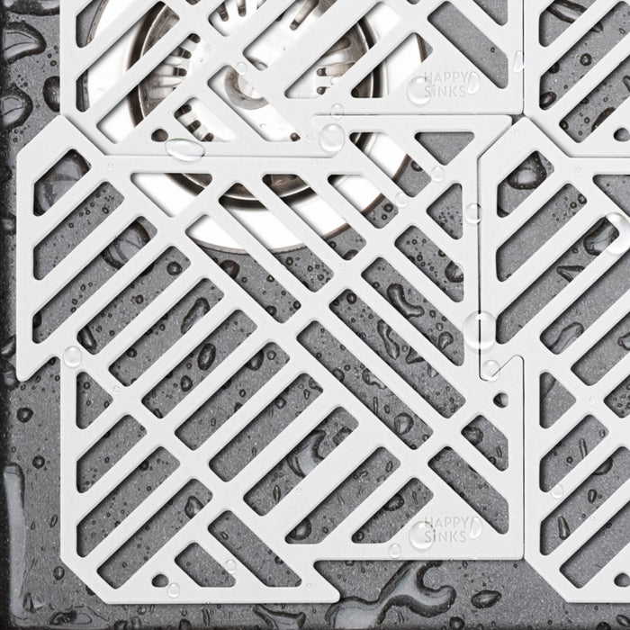 Close-up of a contemporary metal drain cover featuring diagonal cutout patterns. Water droplets grace the textured surface, paired with the Puzzle Sink Mat for a neat kitchen feel. The brand HAPPY SiNKS is noted on the cover.