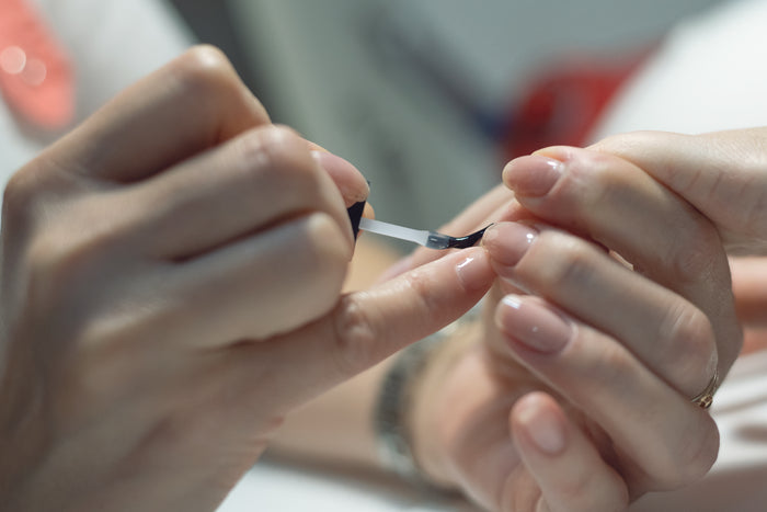 A close-up of someone applying Rugged Beautys Quick Dry Top Coat to another persons neatly manicured nails, with both sets of hands visible.