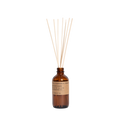 The P.F. Candle Co. Reed Diffuser, in a brown glass bottle with reed sticks, features an elegant black label. It releases a soothing teakwood and tobacco fragrance against a pristine white background, offering an aromatic escape.