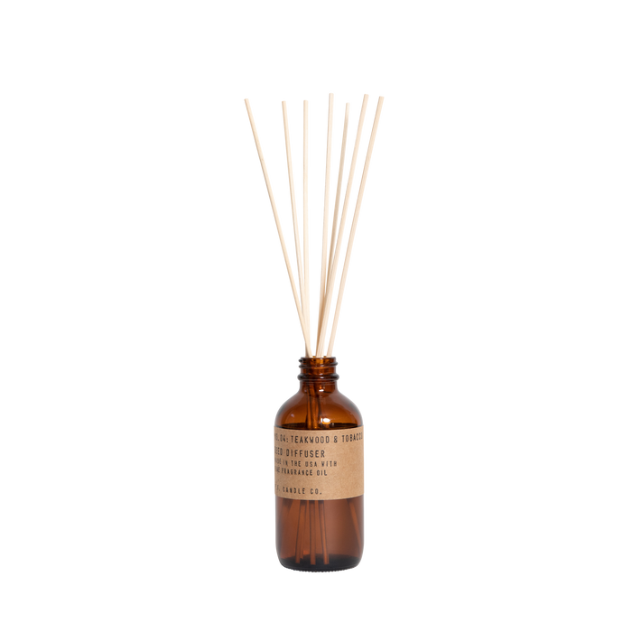 The P.F. Candle Co. Reed Diffuser, in a brown glass bottle with reed sticks, features an elegant black label. It releases a soothing teakwood and tobacco fragrance against a pristine white background, offering an aromatic escape.