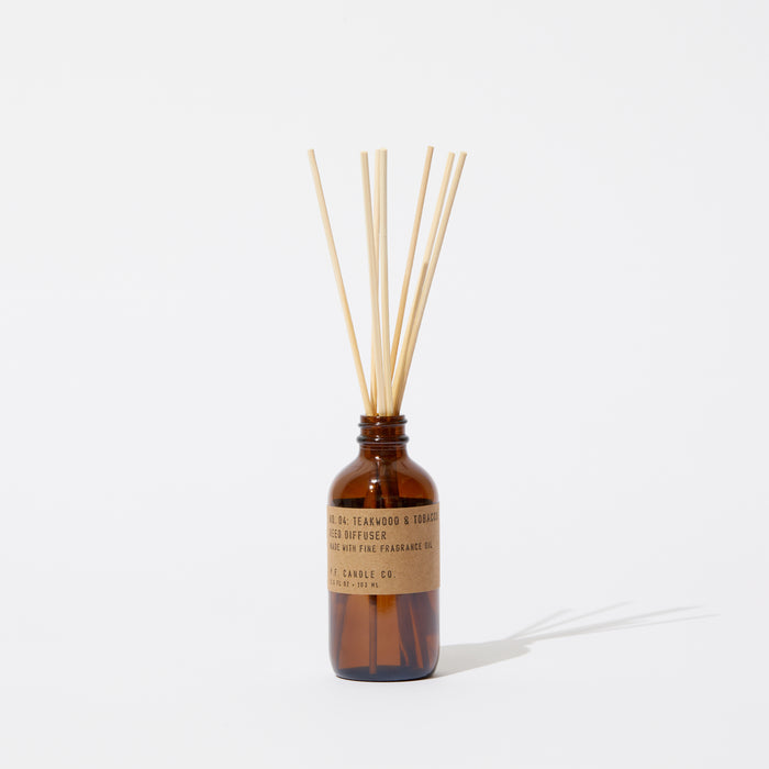 The P.F. Candle Co. Reed Diffuser features a brown glass bottle with a natural paper label, filled with teakwood scent and slender wooden sticks. It is set against a plain white background, casting a gentle shadow.