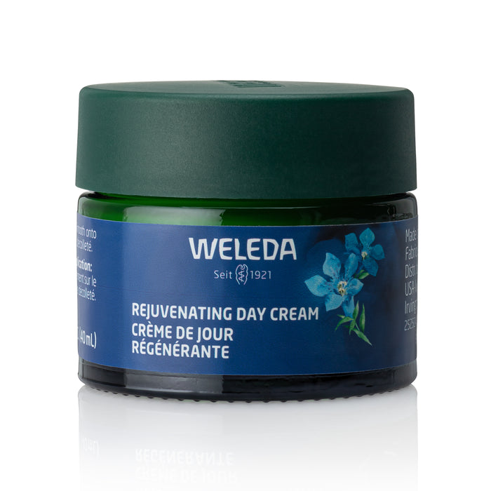 A green glass jar with a dark green lid labeled Weleda Rejuvenating Day Cream for mature skin, featuring a blue flower illustration and bilingual English and French text.