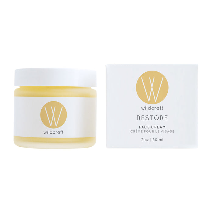 A handcrafted 2 oz (60 ml) jar of Wildcraft Restore Face Cream rests beside its white box, both featuring the gold Wildcraft logo, offering a rich moisturizer for dry skin.