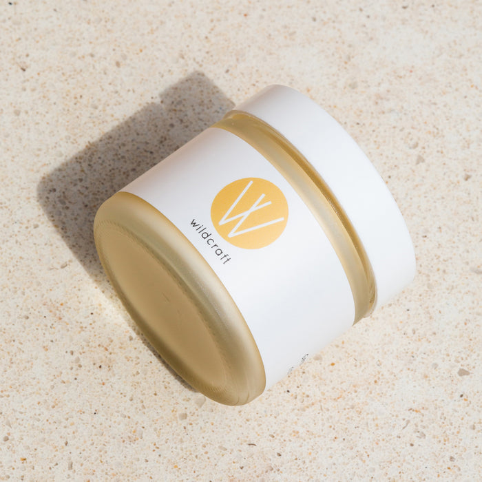 A jar of Wildcrafts handcrafted Restore Face Cream sits on a light textured surface, a moisturizer for dry skin featuring a cylindrical design with a white label that displays a yellow circle and the distinctive W logo.
