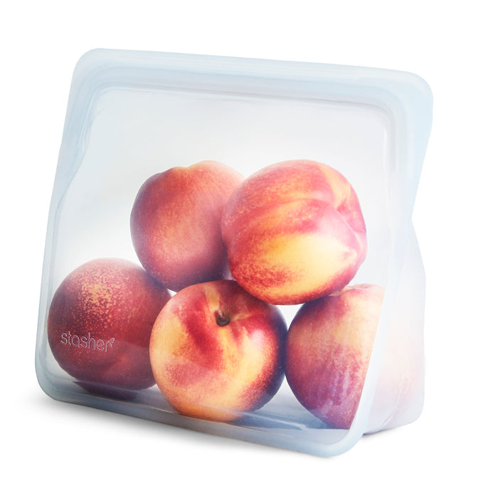 The Reusable Silicone Stand-Up Bag by Stasher, made of eco-friendly silicone, holds six ripe peaches. Its upright, translucent design showcases the peaches clearly, with stasher visible on the front.