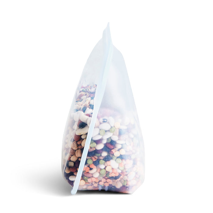 The Stasher Reusable Silicone Stand-Up Bag, shown on a white background, is filled with multicolored pebbles. It features an eco-friendly design with frosted material and a gusseted bottom for extra storage capacity.