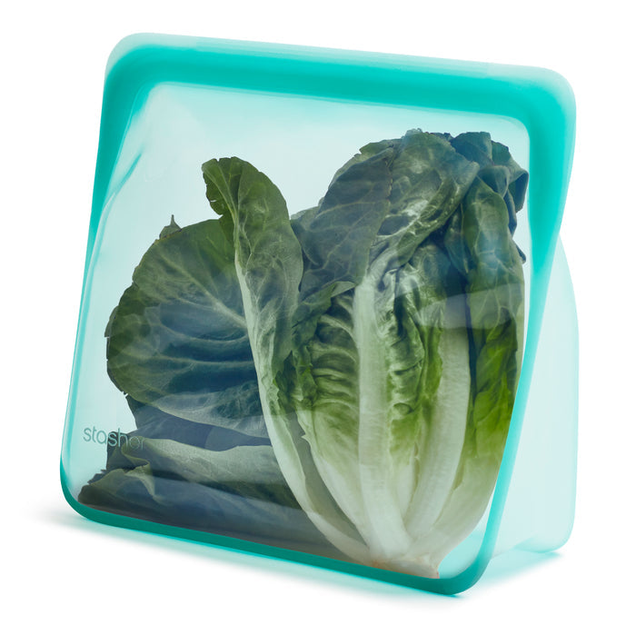 Fresh, green lettuce is stored in a turquoise Reusable Stand-Up Mega Bag by Stasher. This silicone bag with a patented Pinch-Loc™ seal stands upright and remains partially transparent, displaying the crisp texture inside. Its a practical, eco-friendly alternative to plastic.