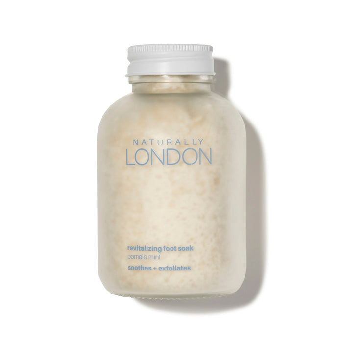 A frosted jar with a white cap and the Naturally London label holds Revitalizing Foot Soak—a pale, grainy powder in pomelo mint scent that soothes, exfoliates, and relieves dry, itchy skin.