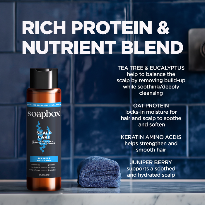 A bottle of Soapbox Scalp Care 2-in-1 conditioner sits on a bathroom counter with a folded blue towel, featuring tea tree, eucalyptus, oat protein, keratin amino acids, juniper berry for fuller hair. Its sulfate-free with biotin B7 benefits.