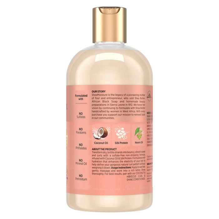 A transparent plastic bottle with a gold cap showcases SheaMoisture Shampoo - Curl + Shine, accented by a peach label. The text highlights key ingredients—coconut oil, silk protein, and neem oil—in addition to a detailed ingredient list and the product story. This curly hair shampoo is an excellent choice for those looking to benefit from nourishing coconut and hibiscus formula.
