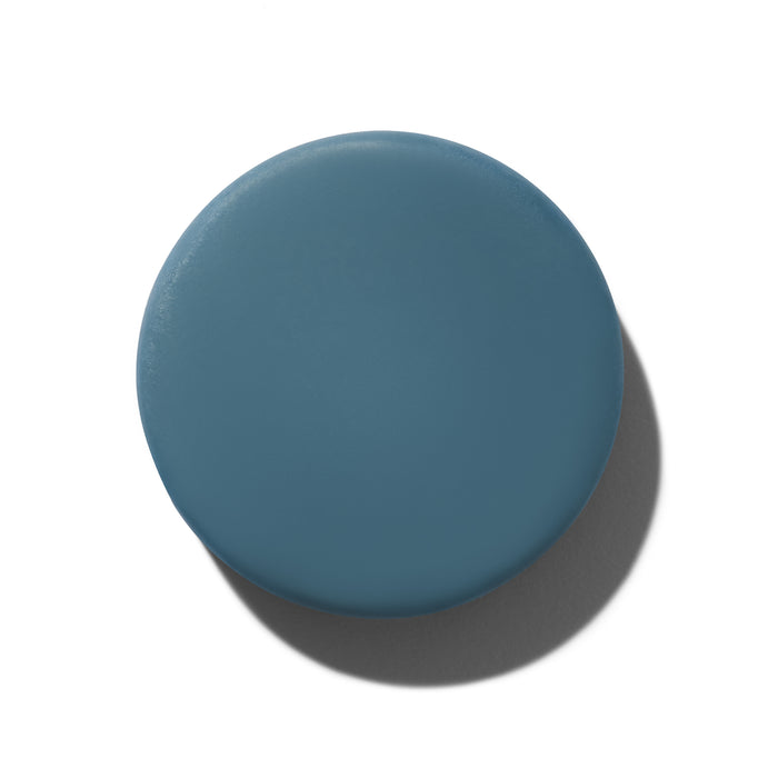 A circular object with a smooth, matte finish in muted teal, reminiscent of NOT!CE Hair Cos Soften Conditioner Bar. It casts a shadow on a white background, suggesting slight elevation and infusion with essential oils. This product is also vegan and cruelty-free.