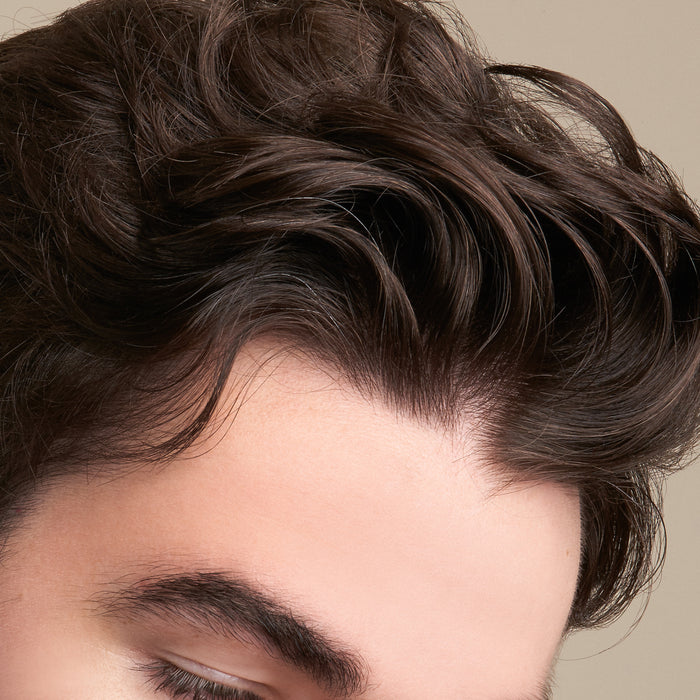 Close-up of a man’s thick, dark brown hair styled in soft waves, enhanced by NOT!CE Hair Cos Soften Conditioner Bar infused with essential oils. The image highlights hair texture and part of the forehead with smooth skin and visible eyebrows against a neutral background.