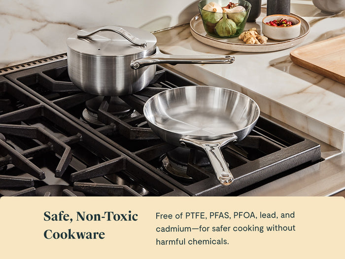 The Caraway Stainless Steel Mini Fry Pan & Mini Sauce Pan Duo sit on a gas stove by a wooden cutting board with mushrooms, herbs, and olive oil. Text reads: Safe, Non-Toxic Cookware—free of harmful chemicals.