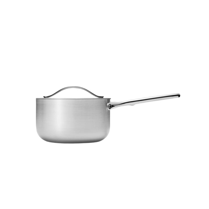 The Caraway Stainless Steel Sauce Pan, 3 qt, is non-toxic with a long handle and matching lid. It features a smooth brushed finish and gently curved lid handle. With 5-ply construction, its oven-safe, fitting versatile cooking needs against a plain white backdrop.