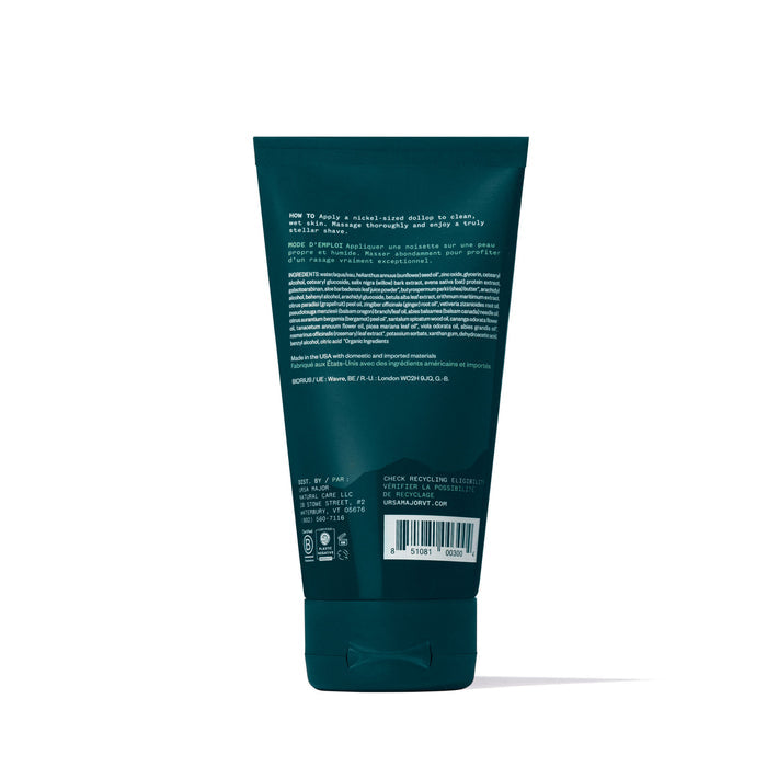 A dark green squeeze tube of Ursa Major Stellar Shave Cream, shown from the back. The label lists instructions, ingredients, and details in small print. A barcode appears near the base above the cap on this non-lathering, botanical-scented formula.