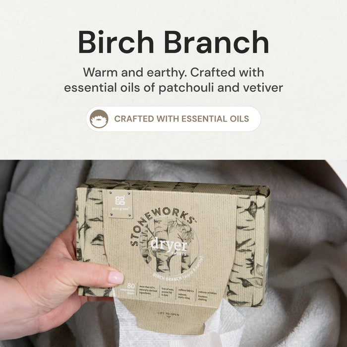 A hand pulls a dryer sheet from a box of grab green Stoneworks Dryer Sheets - Birch Branch. The package features leaf illustrations and metallic accents, with text: Warm and earthy. Crafted with essential oils of patchouli and vetiver to reduce static cling.