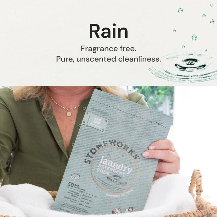 A woman in a green shirt holds Stoneworks Laundry Detergent Pods - Rain by grab green, known for deep cleaning, above white towels. The package says Fragrance Free with a raindrop illustration and highlights its EPA Safer Choice Certification.