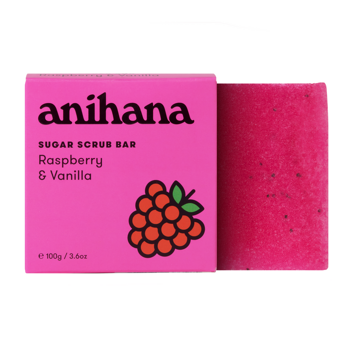 A pink Anihana Sugar Scrub Bar box, decorated with raspberry illustrations, is next to the matching bar speckled with black dots. Infused with coconut oil for gentle exfoliation in raspberry and vanilla scents, this scrub delights your skin.