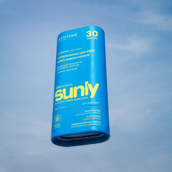 A blue ATTITUDE Sunly Sunscreen Stick for Kids SPF30, labeled plastic-free and vegan, floats against a light blue sky background.