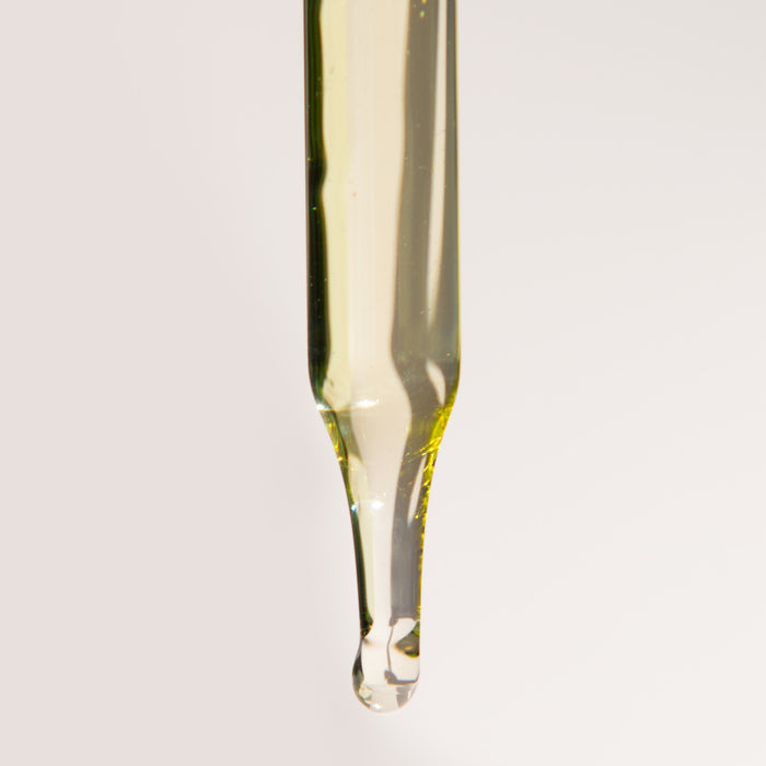 A close-up of a dropper with a droplet of pale yellow liquid against a light background captures the essence of premium oils, perfect for enhancing your Terra Floral Love Bath Experience Gift Set by Terra Beauty Bars.