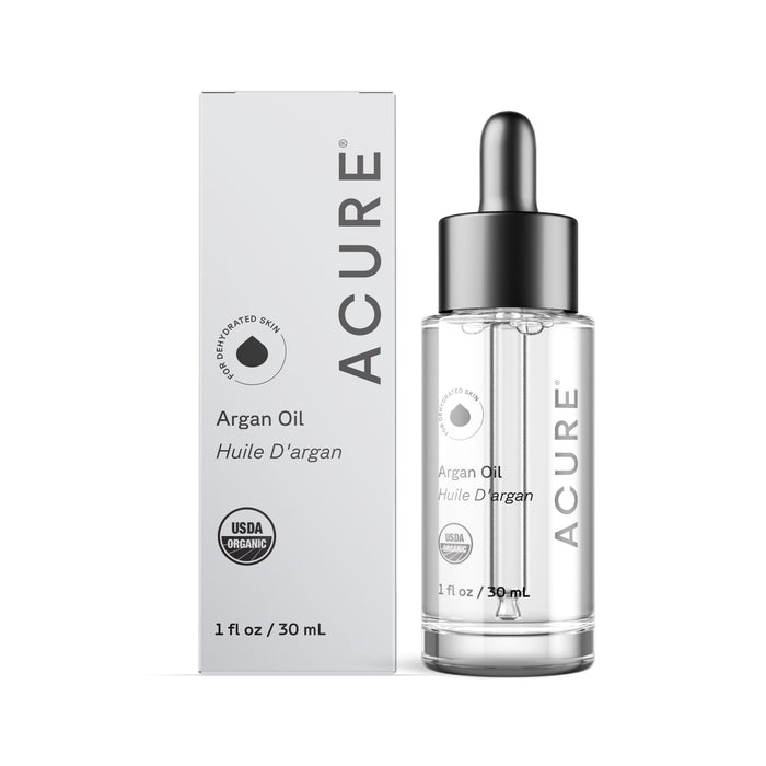 A bottle of Acure The Essentials Argan Oil (1 fl oz / 30 mL) with a dropper top is shown beside its white box. The packaging highlights it as a Skin Superfood and displays the USDA Organic certification.