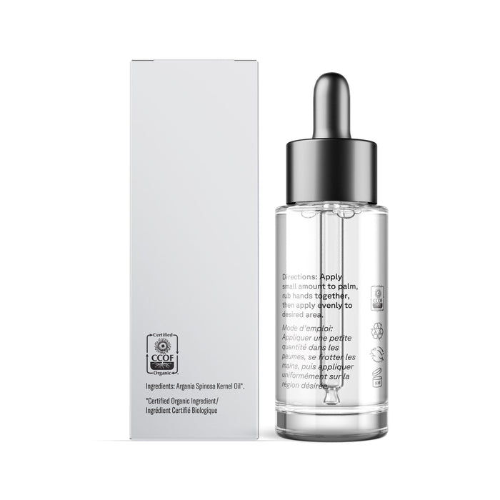 A clear glass dropper bottle with a silver cap, filled with The Essentials Argan Oil by Acure, stands beside a white box. Both feature black text with product info and certification icons, highlighting its vegan skincare benefits.