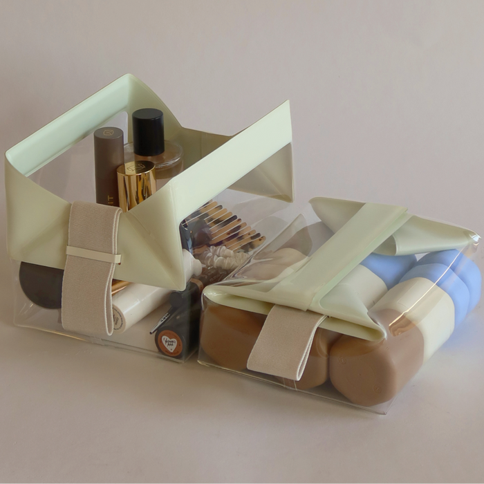 Two transparent TSA-approved travel bags from Cadence, called The Parcel, feature light green flaps and beige straps, filled with assorted cosmetics—ideal for any magnetic travel system from this women-owned AAPI brand.
